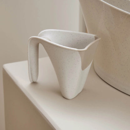 Small jug with curved handle resting on a bathroom shelf beside a baby bath.