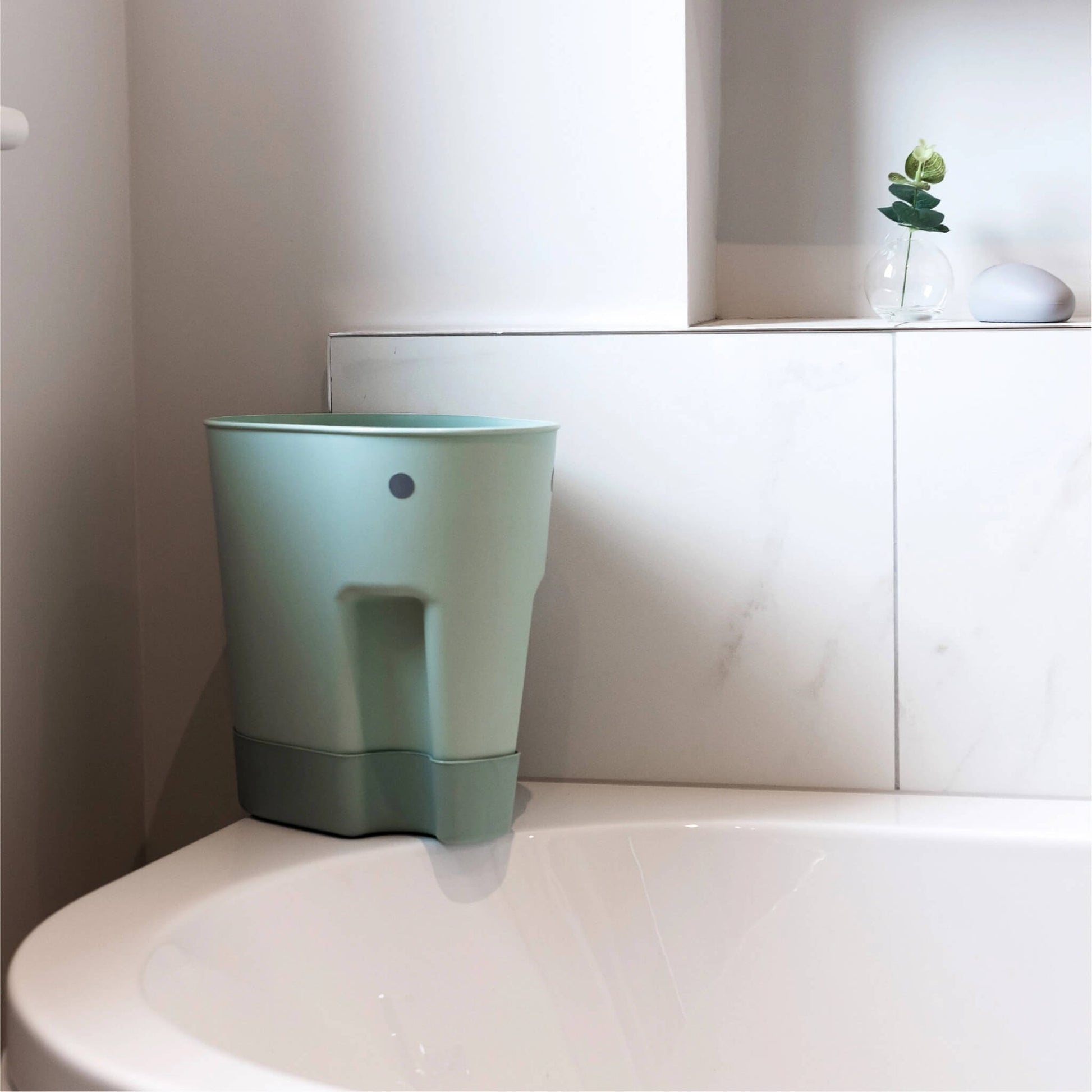 A bath toy drying caddy in eucalyptus green positioned beside a bathtub, showing compact freestanding storage between uses.