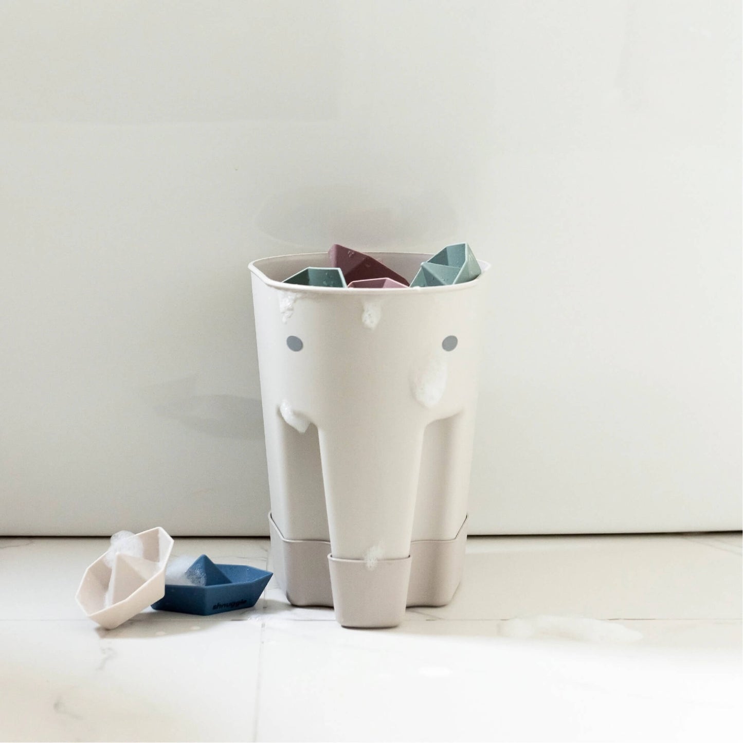 Elephant-shaped bath toy drying caddy holding pastel bath toys, with water droplets visible on the outer surface.