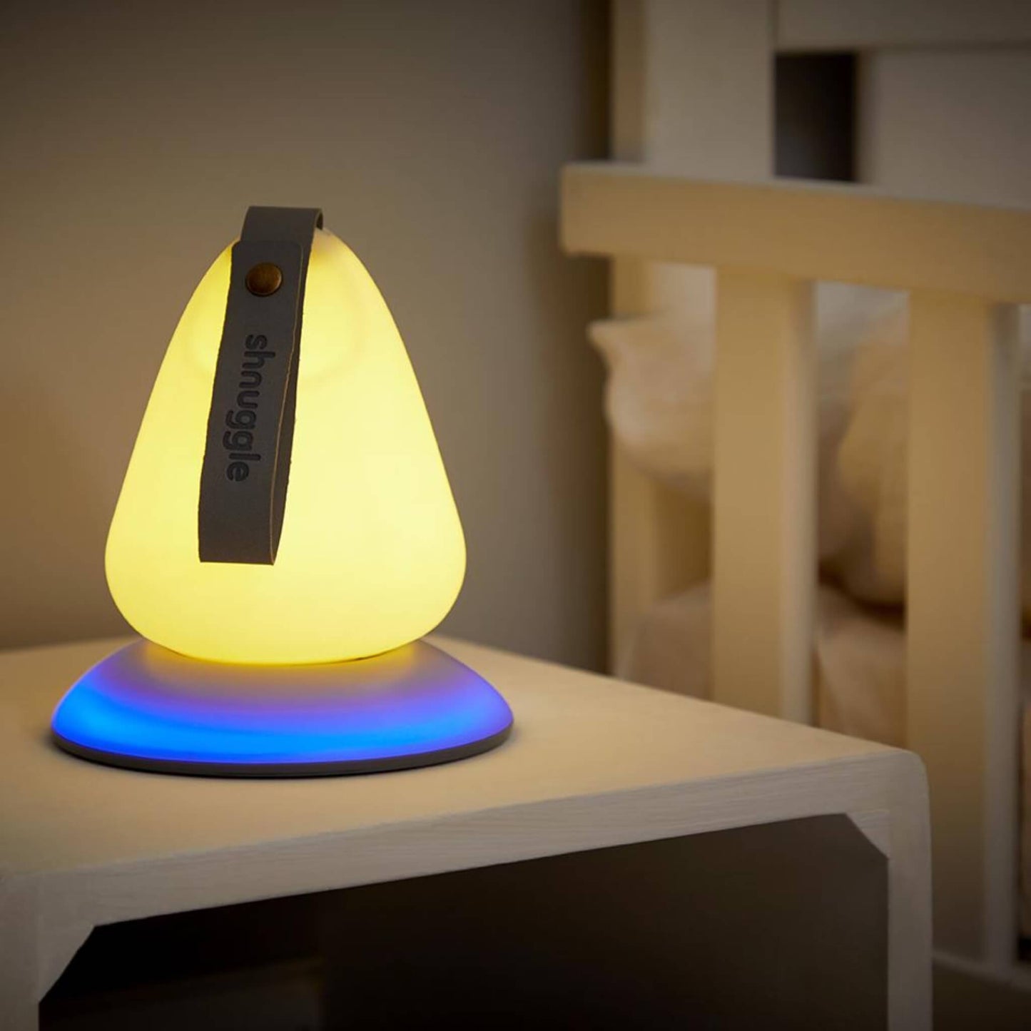 Nightlight glowing yellow with a blue base light beside a cot in a softly lit bedroom.