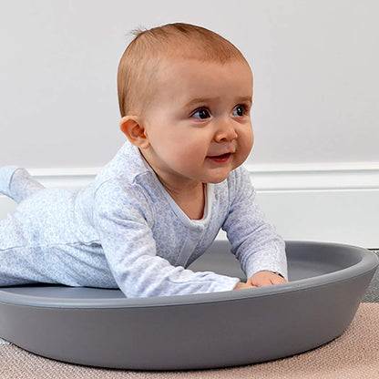 Changing Mat in grey with a baby lying on their tummy, showing the raised cushioned sides and contoured foam design on a carpeted floor.