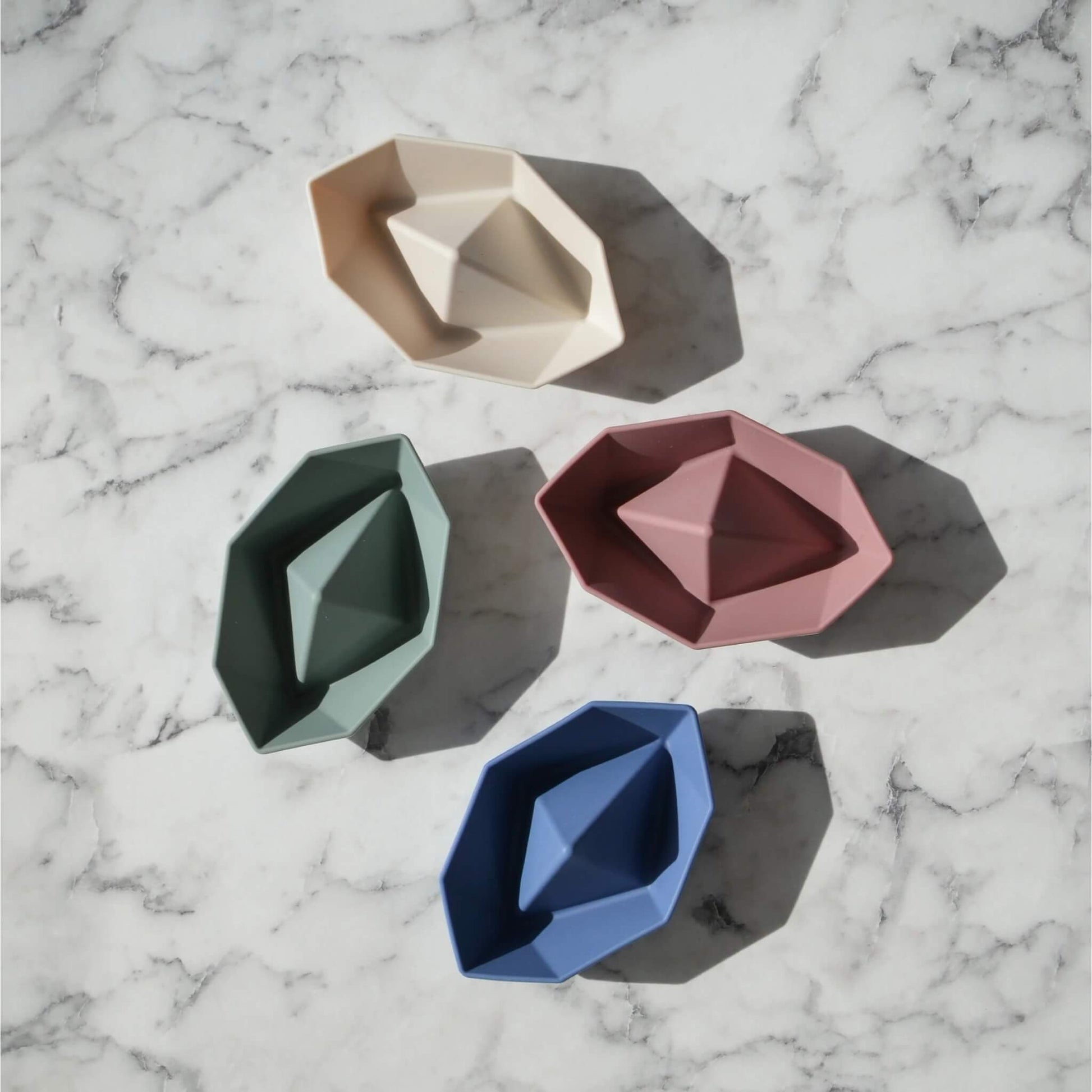 Four small boat toys arranged on a flat surface, photographed from overhead to show shape and form.