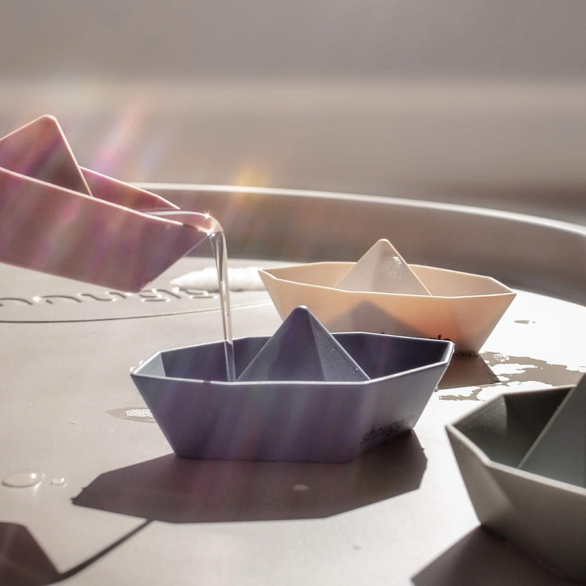 Bath boats placed on a changing mat surface while water is poured into one boat, showing filling and pouring play.
