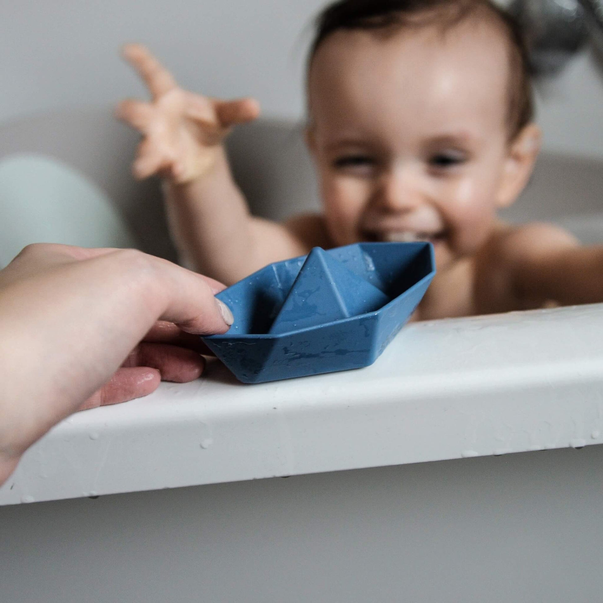A close-up view of a blue bath boat held towards a baby’s hand, showing smooth edges and simple shape.