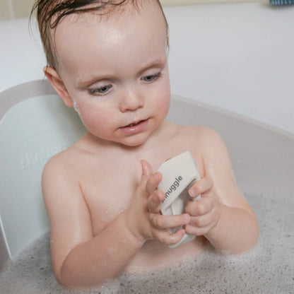 A baby squishing a bath boat while seated in a baby bath filled with bubbles.