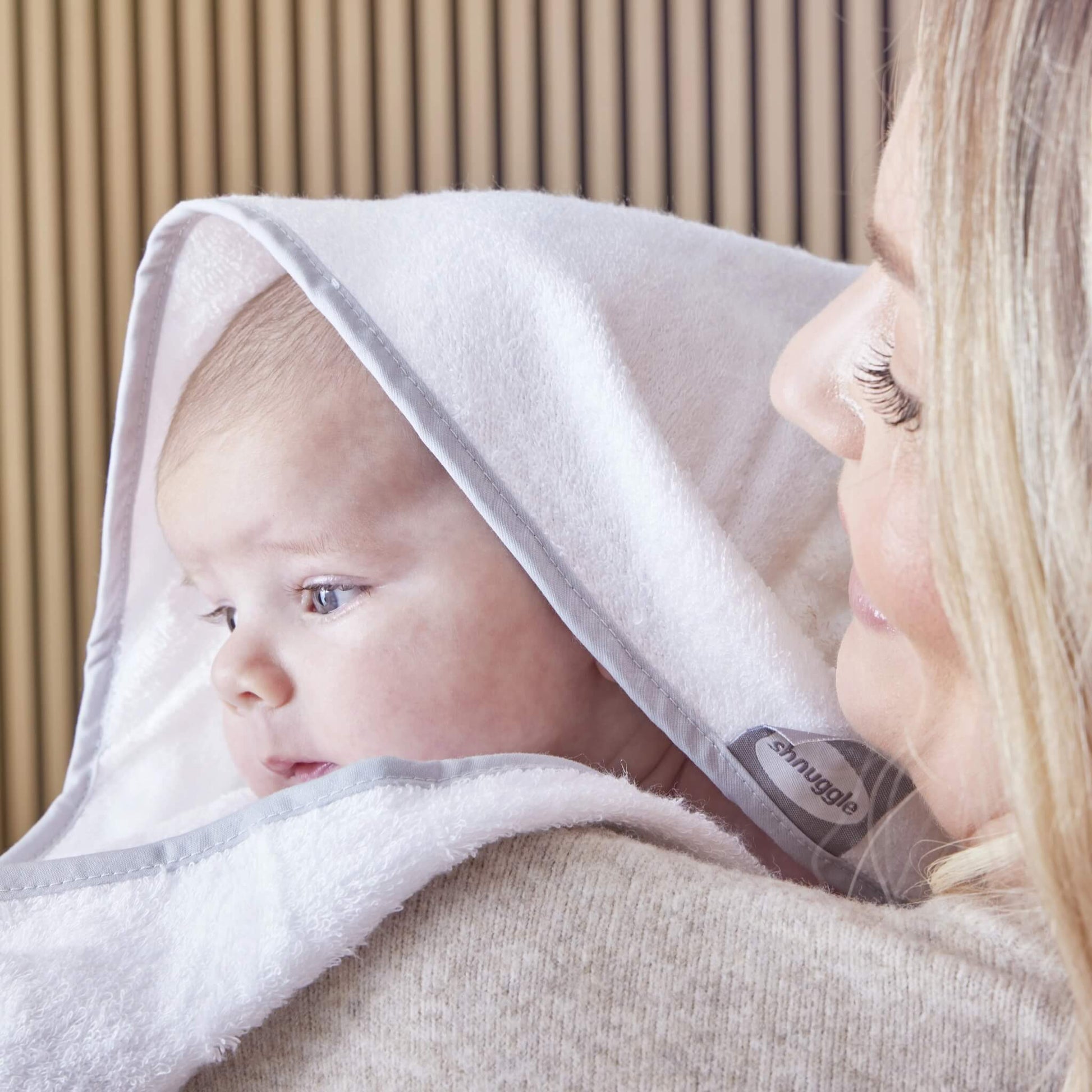 A baby wrapped in a hooded towel, held close by a mother after bath time.