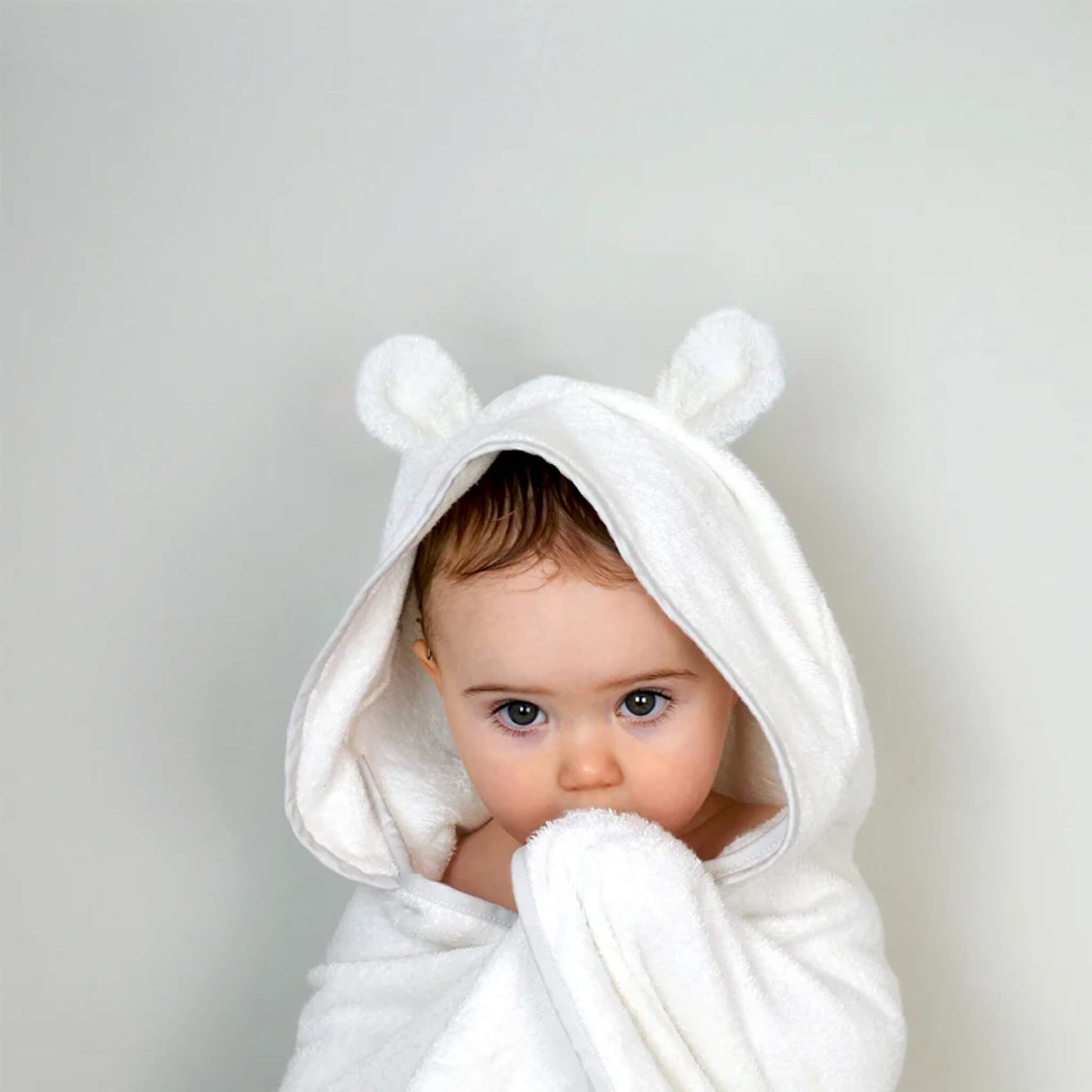 A baby wearing a hooded towel with small bear ears, looking forward while wrapped securely after a bath.