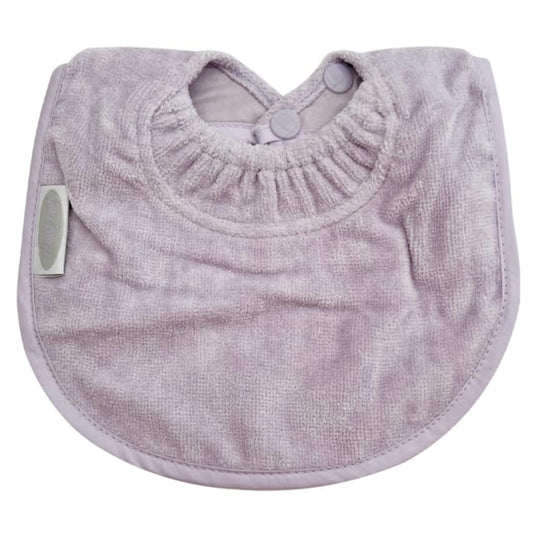 Silly Billyz Towel Biblet in a soft lavender tone, showing a compact newborn bib with an absorbent towelling front, curved shape, stitched edging, and a double snap neck closure.