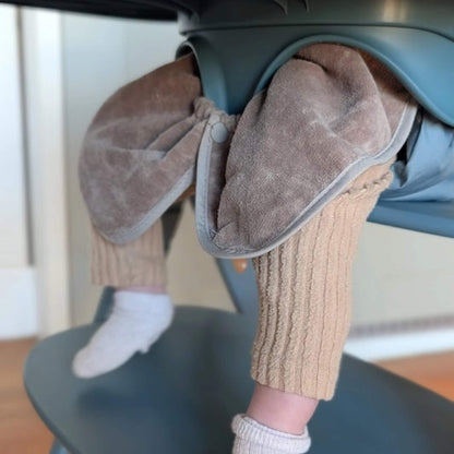 A close-up view of a taupe towel bib fastened underneath a highchair tray, showing the snap closure and gathered towelling fabric designed to catch food and spills.