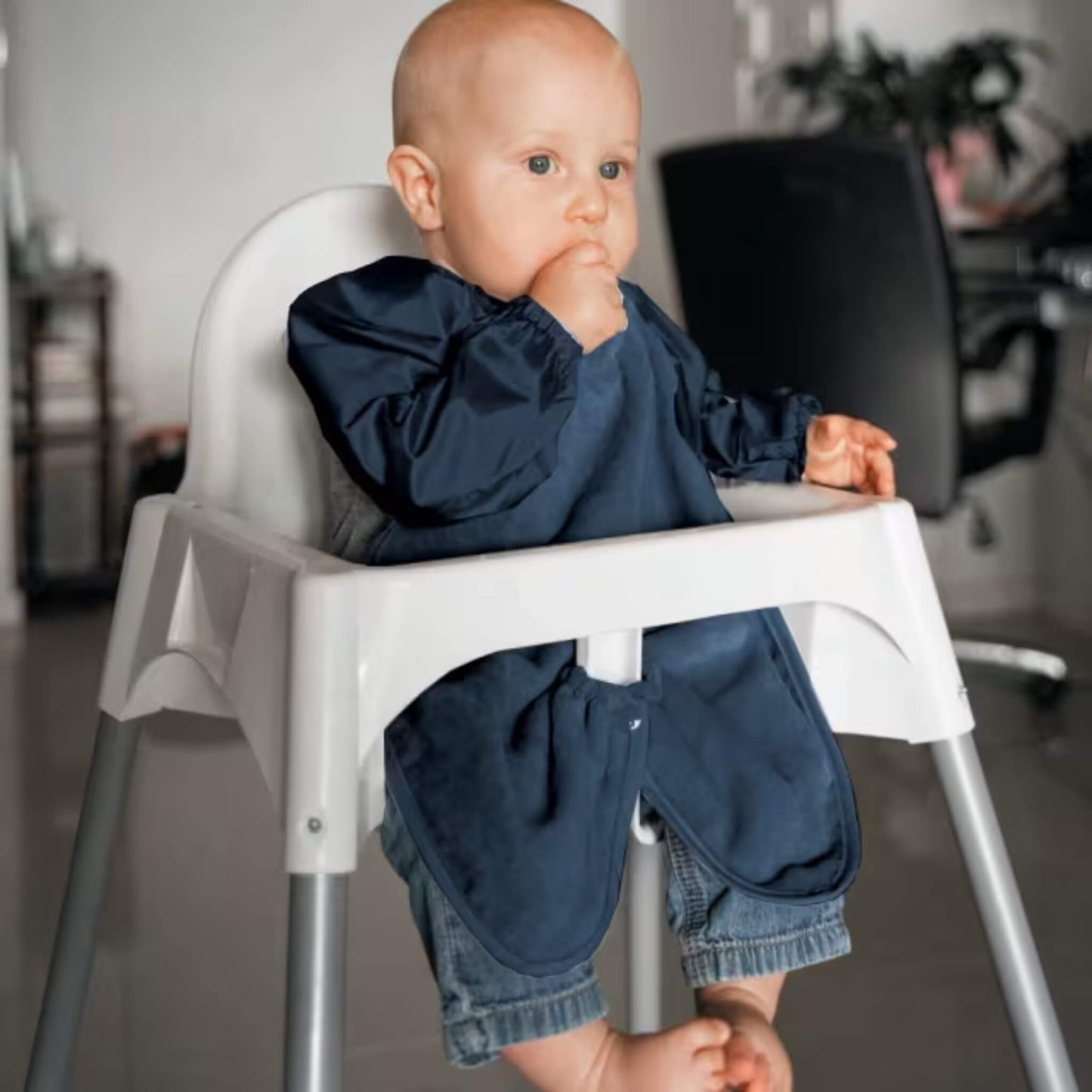 A baby wearing a long sleeve navy highchair bib while sitting in a highchair, showing full arm coverage, soft towel front and elasticated cuffs during feeding.