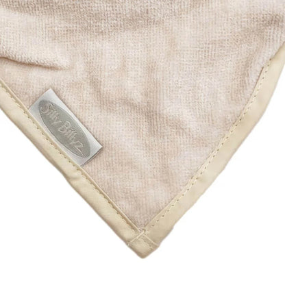 A detailed view of the pointed tip of a cream bandana dribble bib, showing soft towelling fabric with stitched edging and fabric logo tag.