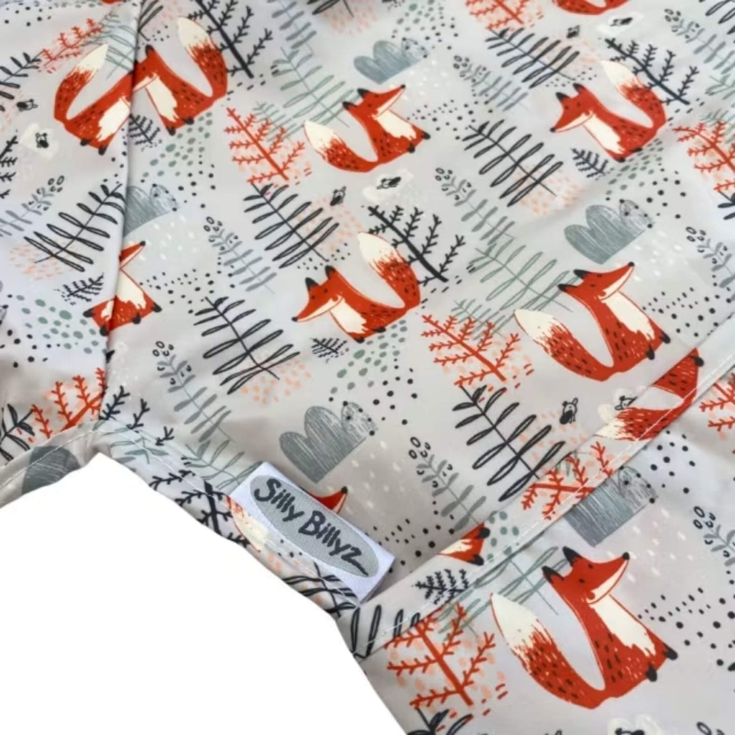 A close-up of a wipe-clean bib featuring foxes and simple woodland shapes, showing the printed surface, stitched seams and pocket edge.