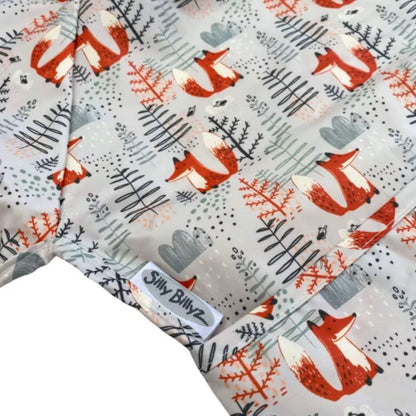 A close-up of a wipe-clean bib featuring foxes and simple woodland shapes, showing the printed surface, stitched seams and pocket edge.