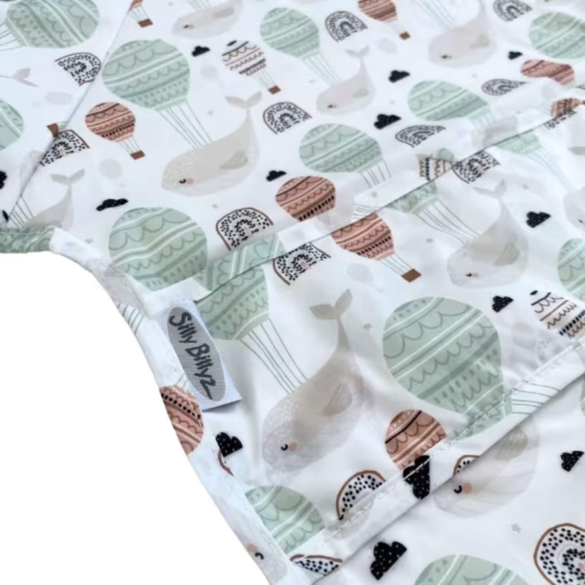 Close-up view of wipe-clean fabric showing the Floating Whales print with hot air balloons, rainbows, and soft neutral tones.