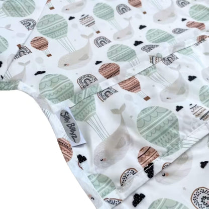 Close-up view of wipe-clean fabric showing the Floating Whales print with hot air balloons, rainbows, and soft neutral tones.