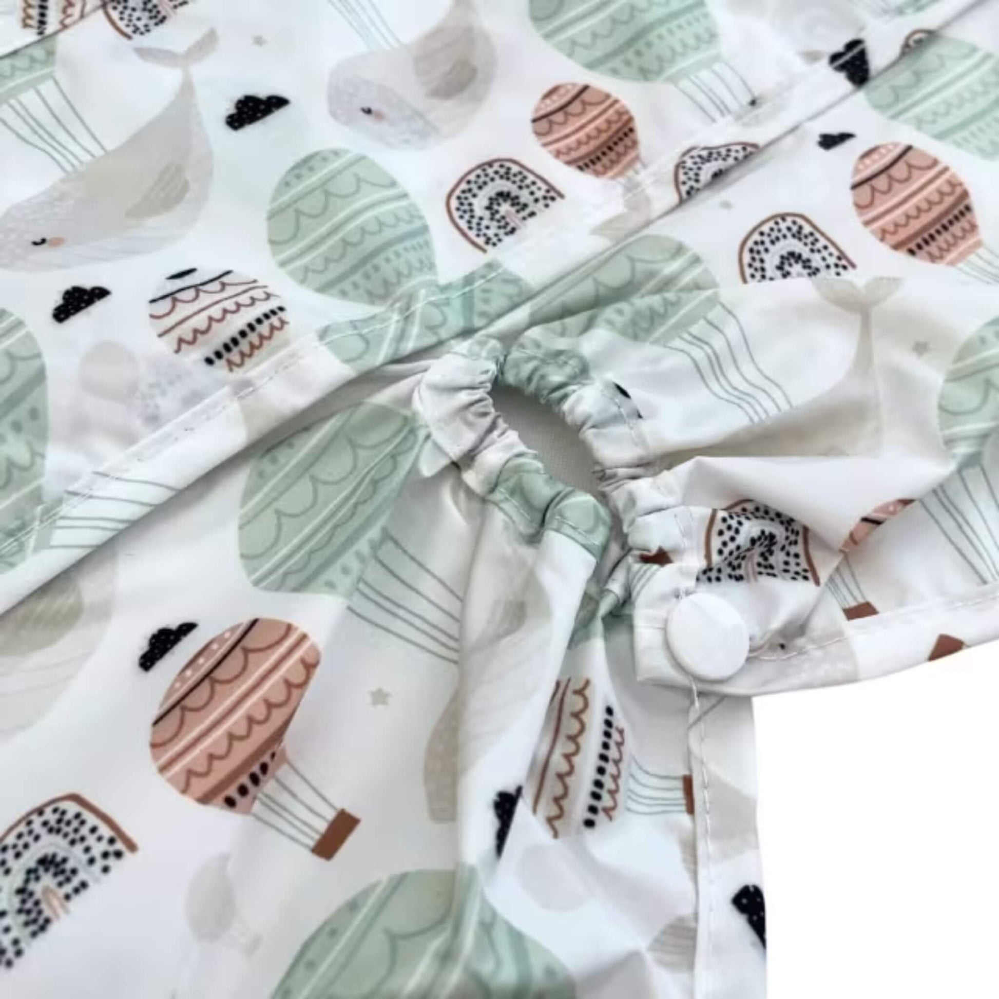 Close-up of the highchair attachment opening with elasticated edge and popper fastening, showing how the bib secures around the chair.