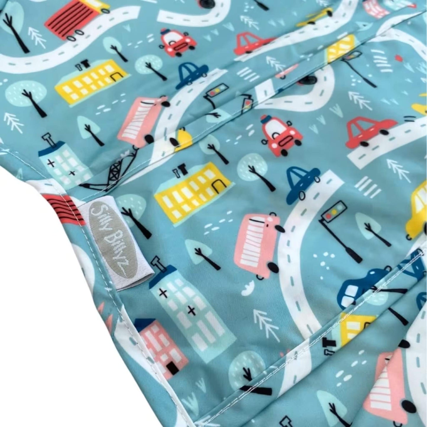 Close-up of a wipe-clean nylon long sleeve highchair bib showing the Roadmap print with illustrated roads, cars, buildings, and trees in soft blue, yellow, red, and white tones.