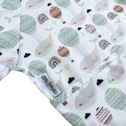 Close-up of wipe-clean baby bib fabric showing floating whale and balloon print with stitched edging and sewn-in brand label.