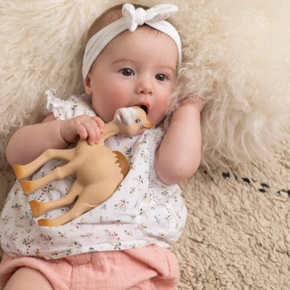 A baby lying on a textured rug, holding and chewing a camel-shaped natural rubber teething toy during calm playtime.
