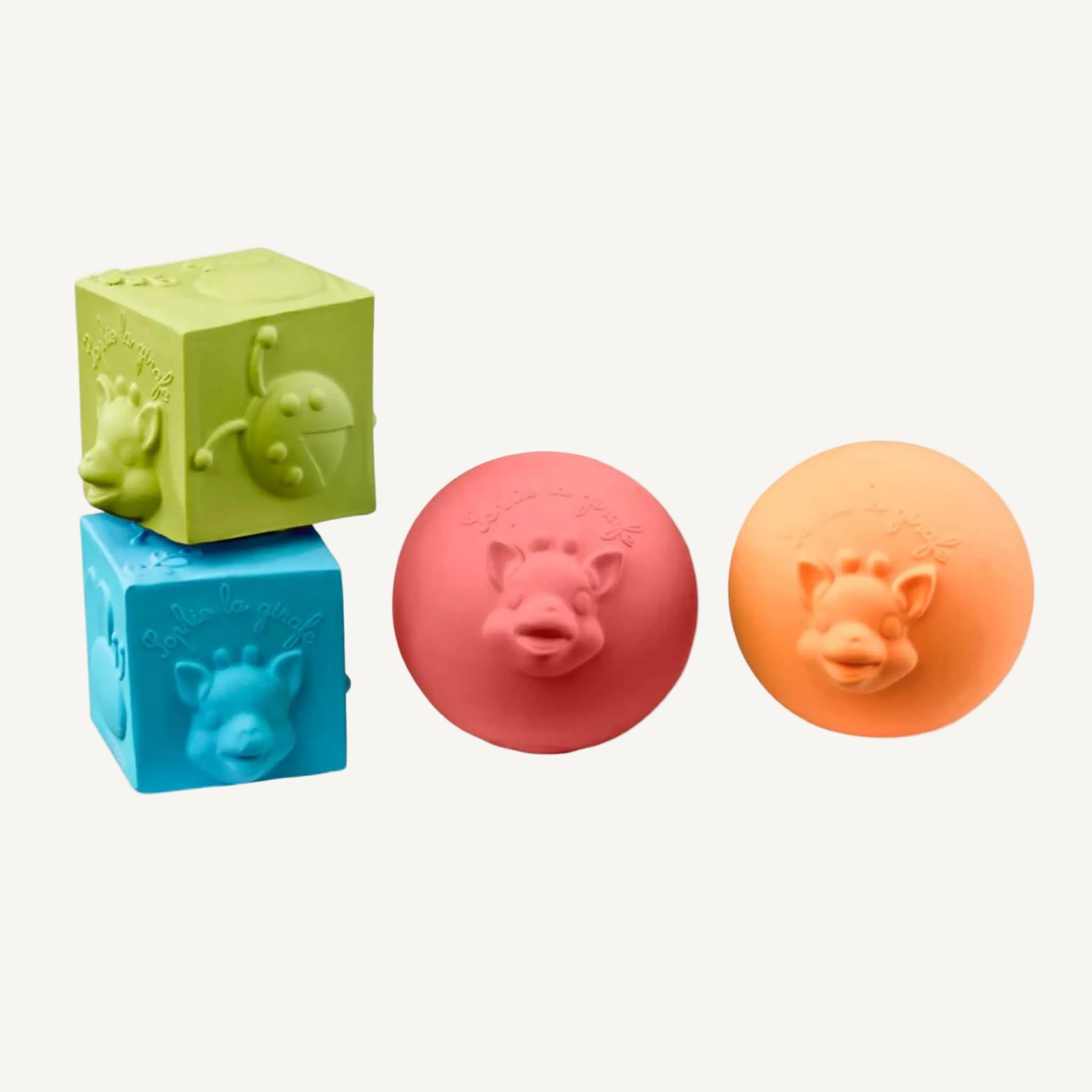 A set of four natural rubber sensory toys including two textured balls and two embossed cubes in soft coral, mustard, blue, and green tones.