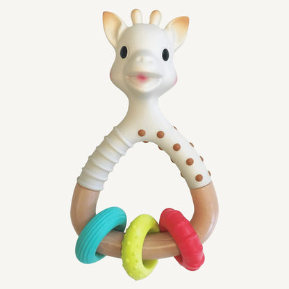 A giraffe-shaped natural rubber rattle teether with a curved handle and three textured rings in teal, yellow, and red attached at the base.