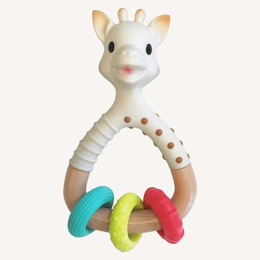 A giraffe-shaped natural rubber rattle teether with a curved handle and three textured rings in teal, yellow, and red attached at the base.