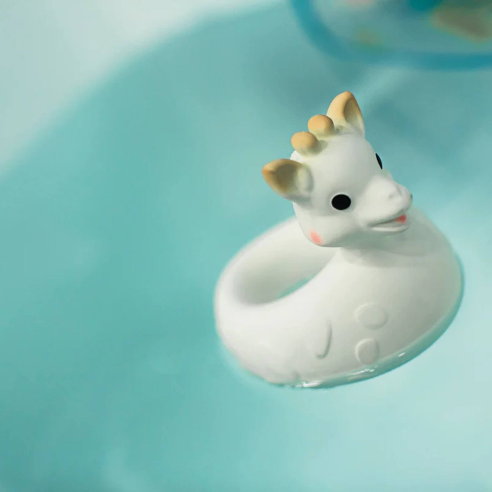 Close-up of a floating giraffe bath toy resting on bath water with ripples around it.
