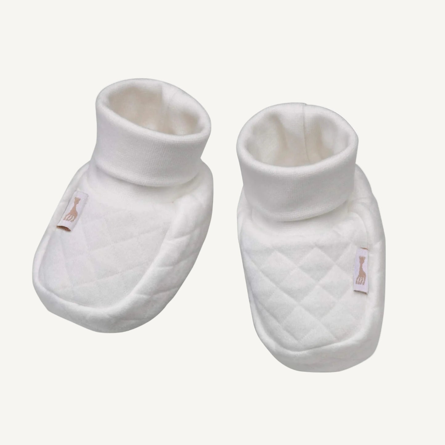 A pair of white quilted newborn booties with soft folded cuffs and subtle stitched detailing.
