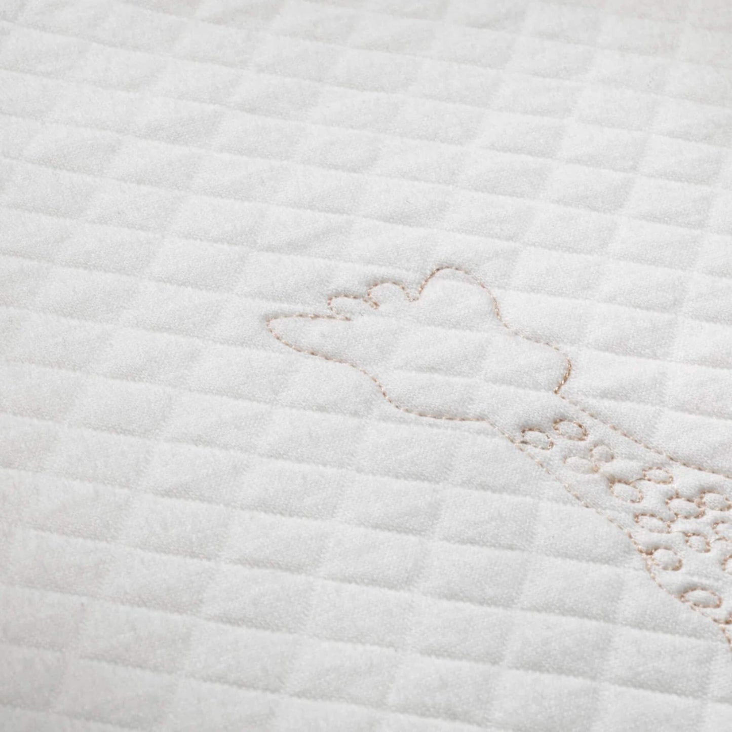 A close-up of quilted white fabric showing stitched giraffe outline embroidery and soft padded texture.