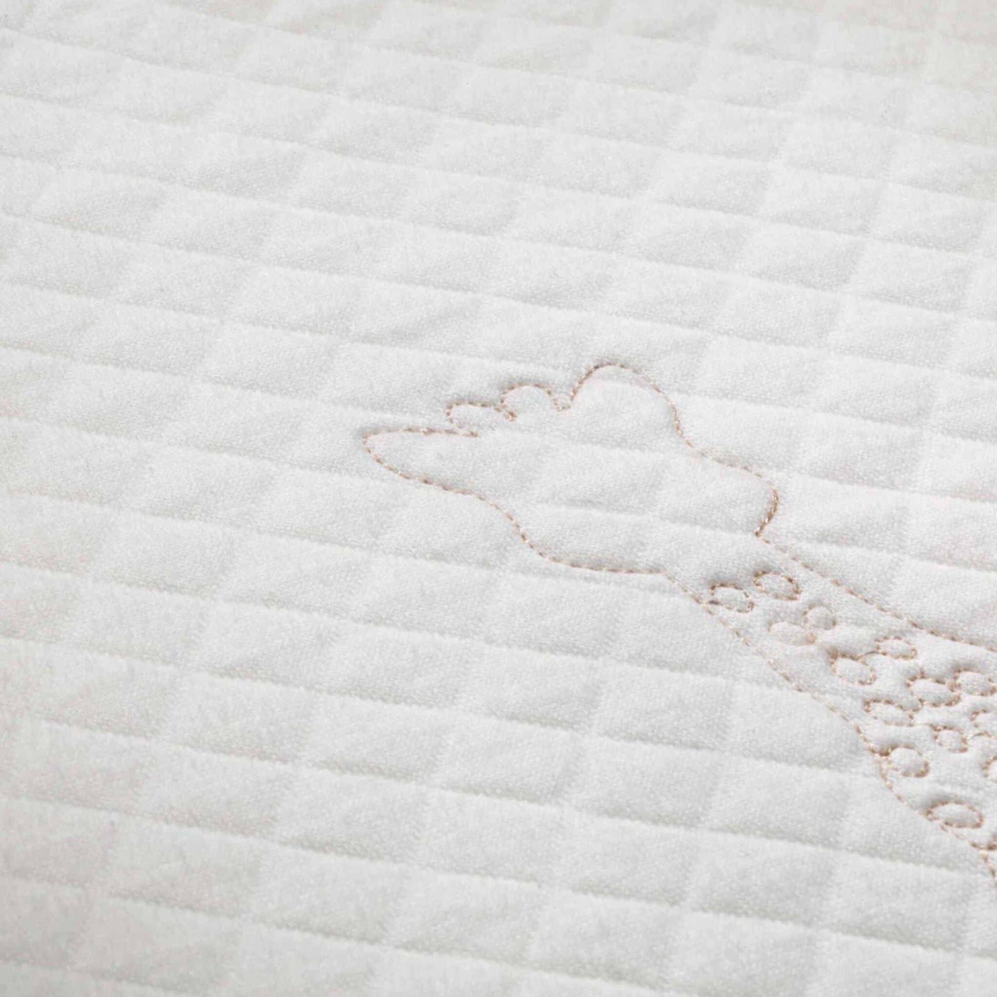 A close-up of quilted white fabric showing stitched giraffe outline embroidery and soft padded texture.