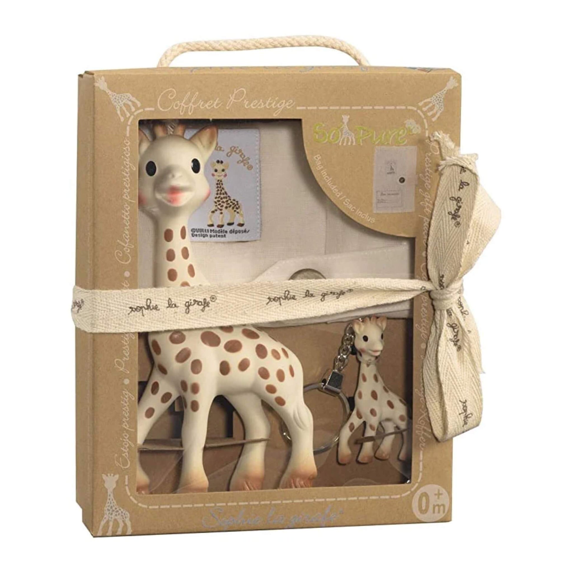 A Sophie La Girafe baby gift set presented in a kraft cardboard box with ribbon tie, showing a rubber giraffe toy, a small giraffe keyring and a fabric keepsake booklet inside a windowed front.
