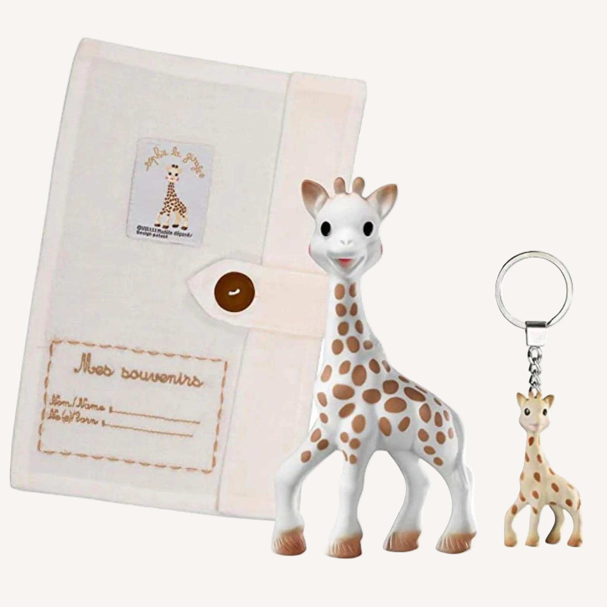 A natural rubber giraffe toy displayed beside a soft fabric keepsake booklet with button closure and a small giraffe-shaped keyring attached to a metal ring.