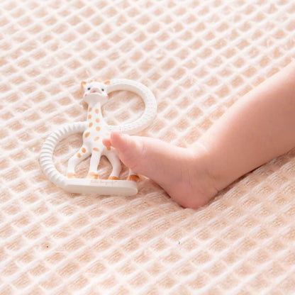 A baby foot resting beside a giraffe-shaped natural rubber teething ring placed on a soft textured blanket.