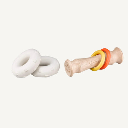 A disassembled view showing two white natural rubber discs beside a wooden rattle handle with coloured sliding rings.