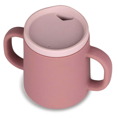Angled view of a dusty pink silicone trainer cup with two side handles and a recessed rim lid, showing the drinking opening.