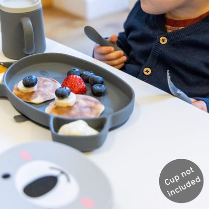 Toddler using grey silicone bear-shaped plate and cutlery set and cup,  ideal for self-feeding.