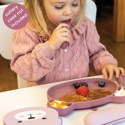 Toddler using pink silicone cutlery and plate with pancakes, fruit, and yoghurt, wearing a pink jumper, perfect for self-feeding.
