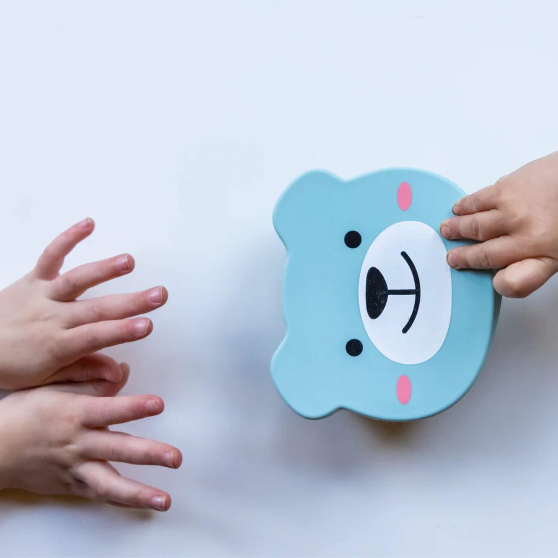 Small hands reaching toward a blue silicone baby bowl with bear-shaped lid secured on top.