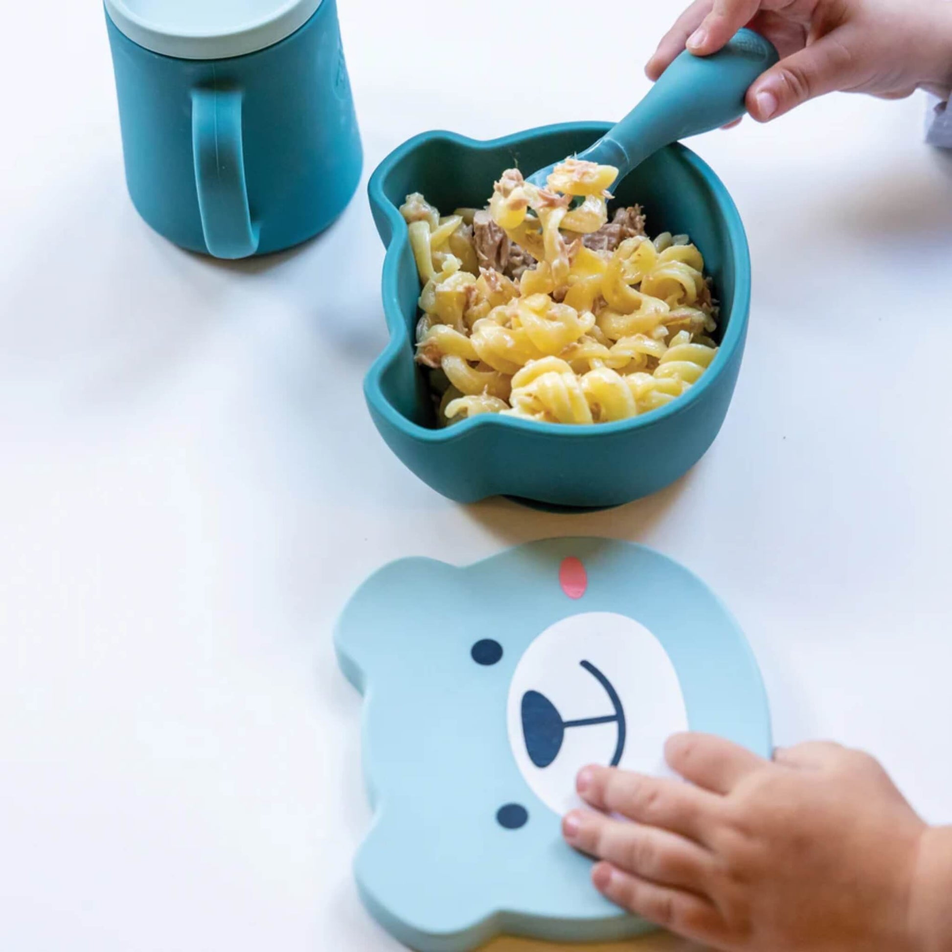Blue silicone baby bowl filled with pasta and sauce, with chunky spoon held above bowl during feeding.
