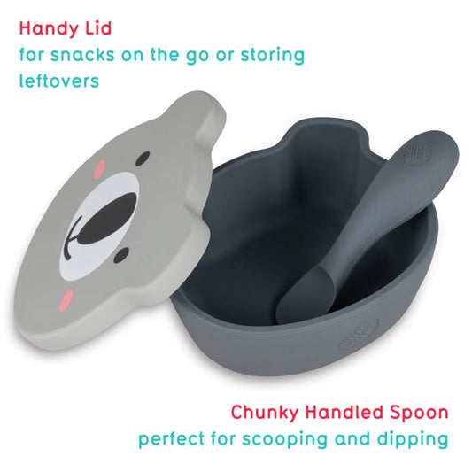 A silicone baby bowl with a bear-shaped lid lifted to reveal the deep interior, with a chunky handled spoon resting inside.