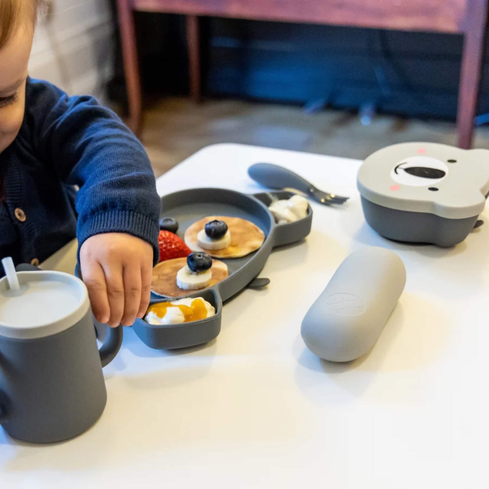 A sectioned silicone plate holding pancakes, fruit and yoghurt, with a small dipping section filled with yoghurt.