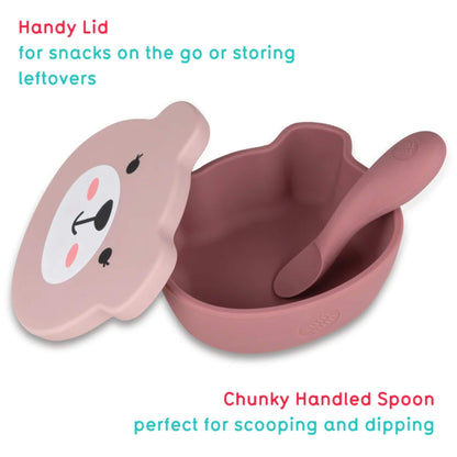 A pink silicone baby bowl with a bear-shaped lid lifted open, showing the deep interior with a chunky handled spoon resting inside.
