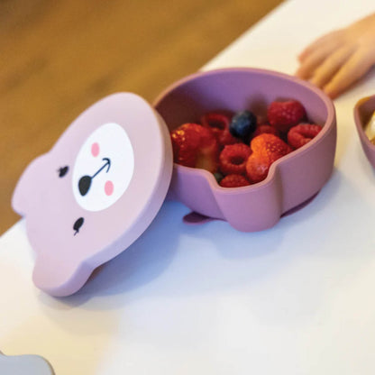 A pink silicone baby bowl filled with fresh berries, shown with the lid placed to one side on a tabletop.