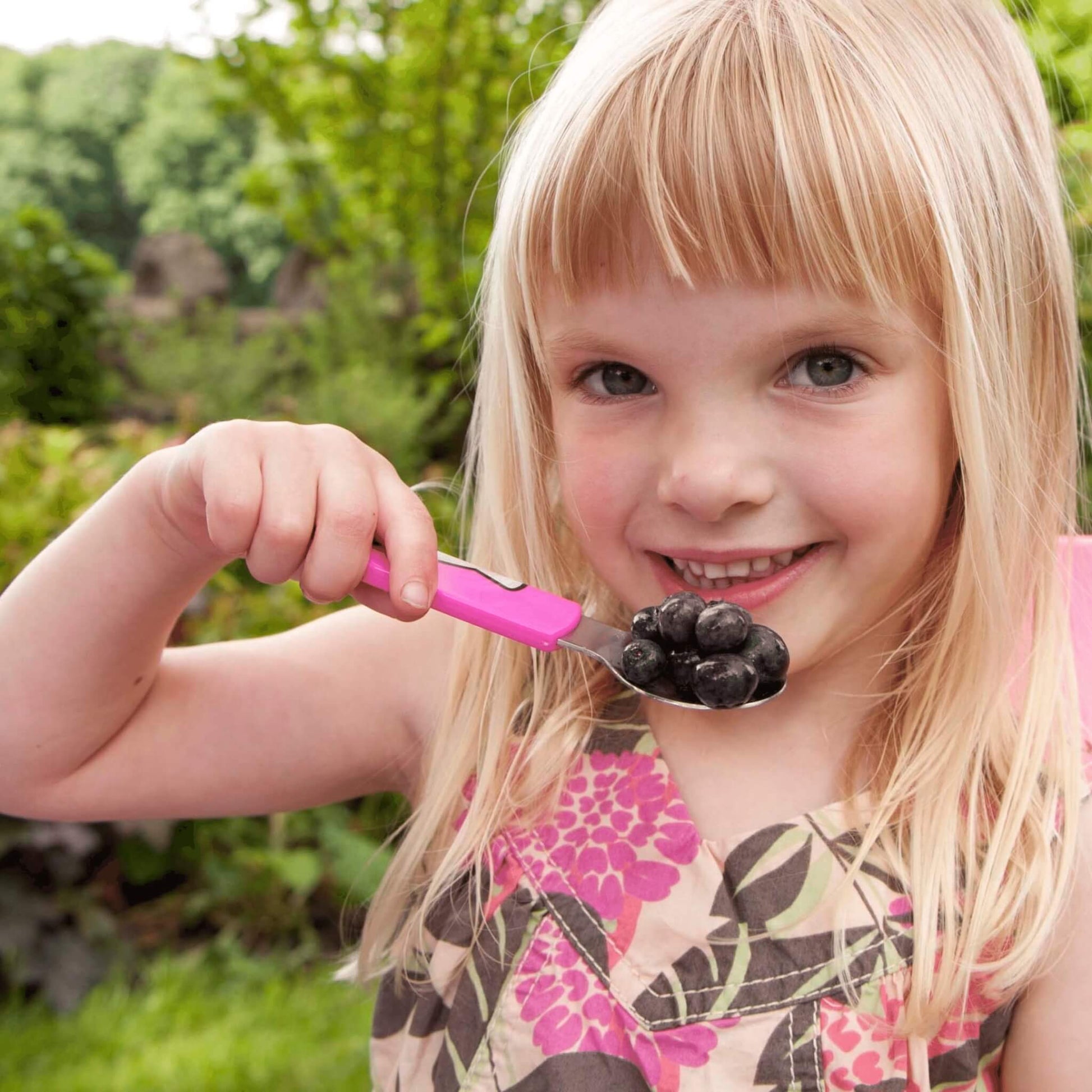 Young girl eating blackberries with a pink spoon outdoors