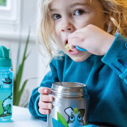 A young child wearing a teal fleece sweater is shown drinking from a stainless steel tumbler with a cartoon frog design. A matching blue water bottle is visible on the left, set against a bright, softly blurred indoor background.