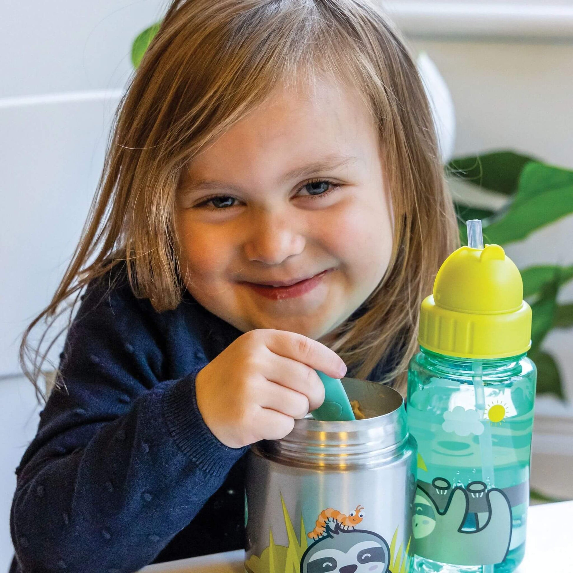 Smiling child enjoying a meal using an insulated food flask and water bottle featuring a cute sloth design, perfect for kids' lunches.