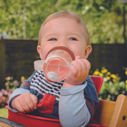 A toddler holding the a orange brown fox cup and drinking from it outdoors.