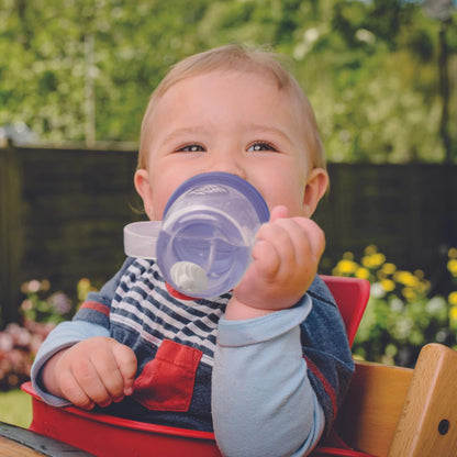A toddler holding the purple owl cup and drinking from it outdoors.