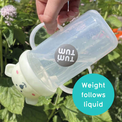 Hand holding a sippy cup tipped sideways outdoors, showing the weighted straw resting at the lowest point so liquid can be drunk from any angle.