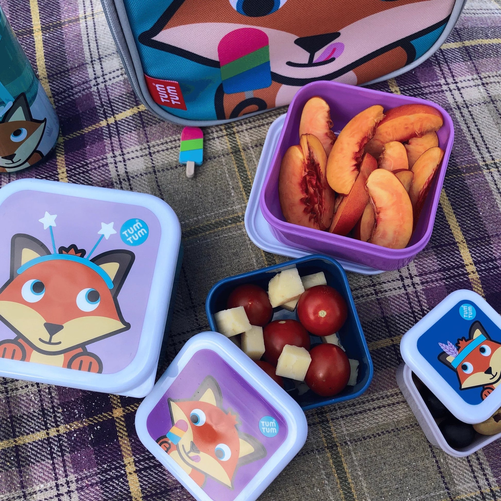 Group of several nesting snack pots with Felicity Fox designs, filled with peaches, tomatoes, cheese, and olives, perfect for kids' snacks.